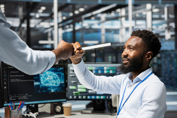 Server room worker greeting colleague, dong fist bump, using AI tools. Engineer saluting coworker,...