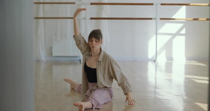 Young girl sitting on floor doing parterre wide stance ballet stretch during classical stretch and sitting in splits in dance studio
