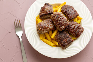 grilled meatballs with penne pasta on a white plate close-up