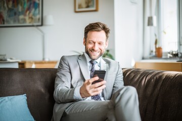 Fototapeta premium Grinning executive on couch using smartphone in office