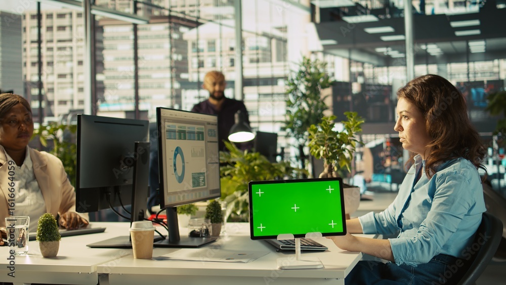 Poster close up of employee sitting at office desk, using green screen tablet to solve tasks during job shi