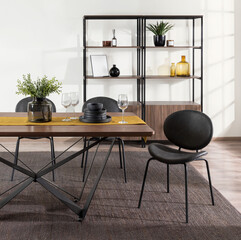 Modern dining room with industrial-style furniture, featuring a rectangular wood table with geometric black metal legs, black leather dining chairs, minimalist shelving, and warm decorative accents.