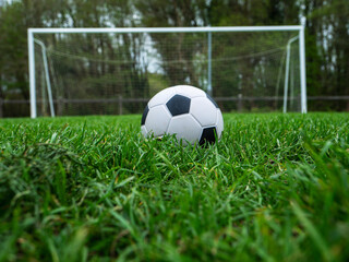 Classic style soccer or football on neatly cut green grass with small training goal posts in the background. Play area in a park. Sport and entertainment concept.