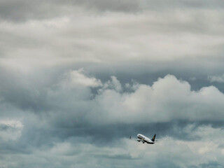 A plane is flying through a cloudy sky. The clouds are dark and heavy, giving the scene a moody and...