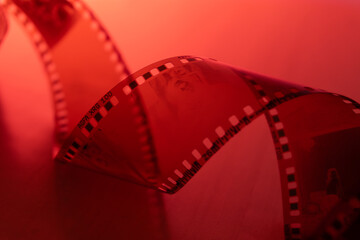 35mm negative photographic film in rotation in red room, camera darkroom. Slightly rolled film strip isolated on red background. Analog film strips. Analog photography. Close-up