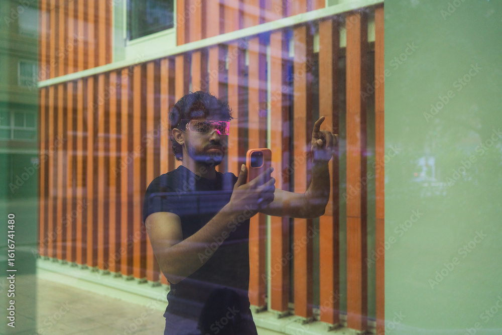 Fototapete latin software developer wearing smart glasses and using smartphone pointing at augmented reality in
