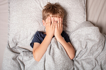 The child was scared before going to bed. Night terrors in a child. The kid covers his face with...