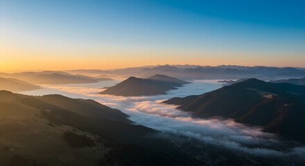 Naklejka premium Morning Mountain Vista: Witness the awe-inspiring moment when the early sun kisses the mountain peaks, with clouds nestled in the valleys below, creating a breathtaking landscape scene.