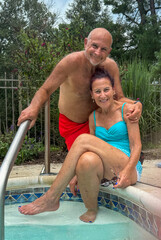 Older senior citizen couple posing together by the steps at the entrance to a swimming pool