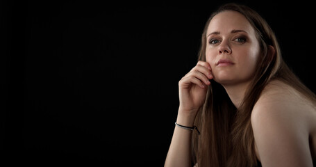 Portrait of a beautiful young woman with long brown hair, posing thoughtfully with her hand on her...