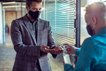 Man wearing face mask using hand sanitizer at office entrance during pandemic