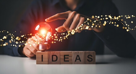 A person's hands holding a glowing lightbulb above wooden blocks spelling "IDEAS" with sparkling light trails.