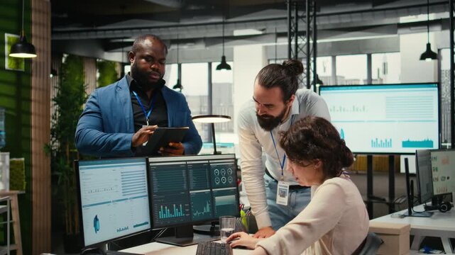 Diverse employees team engaged in business planning and report writing, using company data insights to ensure alignment with objectives. Reviewing reports on computer at the office. Camera A.