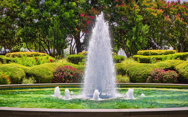 A large fountain with a white spout is surrounded by a lush green garden