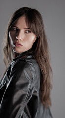 Studio portrait of a beautiful young woman with long brown hair wearing a leather jacket, turning her head and looking over her shoulder