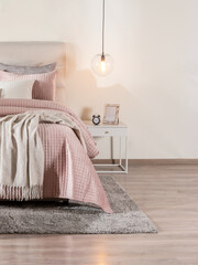 Serene Bedroom Essence Featuring Soft Pink Quilted Comforter on Cozy Bed, Draping Neutral-Toned Throw, Gray Rug Below, Modern Suspended Globe Light Illuminating White Nightstand, Warm Wooden Flooring.