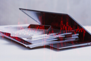 Business tools, laptop with calculator and documents with red graph and downward trend. Concept of financial losses, economic downturns and business problems.