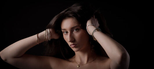 Beautiful young woman holding her long brown hair with her hands wearing bracelets and a necklace...