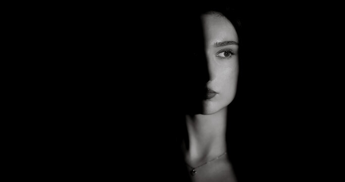 Black and white portrait of beautiful woman with half face illuminated by a light beam