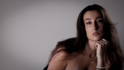 Studio portrait of a beautiful young woman with long brown hair, posing with her hand on her chin,...