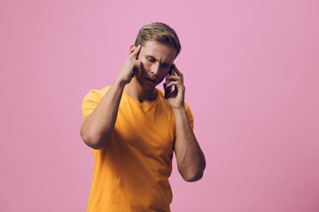 Man with beard talking on mobile phone wearing bright yellow t-shirt against pink background,...