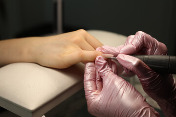 Master in pink gloves in a beauty salon gives a manicure to a client using manicure machine. Close...