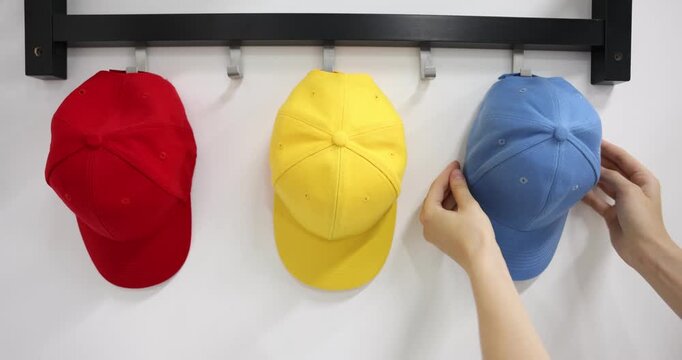 Woman hanging light blue baseball cap onto hook rack on white wall, closeup