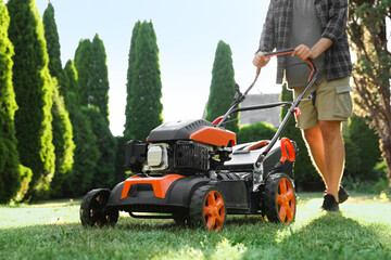 Man cutting green grass with lawn mower in garden, closeup