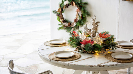 Elegant coastal dining setup with white table and natural Christmas decorations, concept of festive interior styling