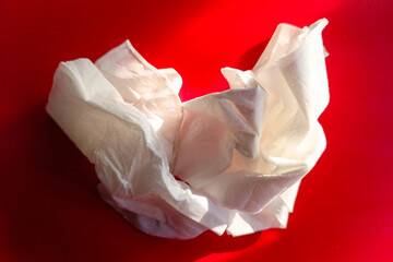 A crumpled white tissue paper rests on a vibrant red surface, illuminated by natural light creating shadows and highlights.