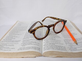 An open Bible with orange pencil and tiger pattern glasses on it.