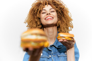Joyful young woman with curly hair holds two delicious burgers showcasing healthy eating choices in a vibrant and cheerful manner