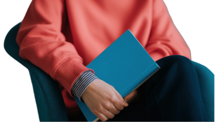 Person in a coral sweatshirt and striped shirt holding a blue hardcover book.