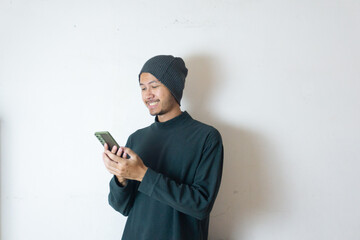 Indonesian man wearing winter clothes laughter while holding phone