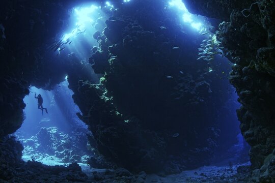 Sunbeams shining through reef top in cave in coral reef with diver, Shaab Claude, Red Sea, Fury Shoals, Egypt