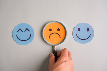 Magnifying glass on sad face and smiling emoticons, mood detection, emotional analysis, and mental health awareness in daily life.
