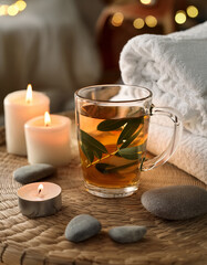 Eucalyptus leaves gently infusing in tall glass of warm herbal tea. Eye-level view from a spa chair, soft candlelight glow, background bokeh of white towels and pebbles, calming muted tones, relaxing 