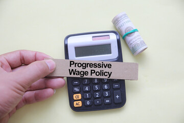 PROGRESSIVE WAGE POLICY Concept with Hand Holding Sign, Calculator, and Rolled Dollar Bills –...