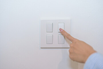 Female finger pushing for turn on light switch on white wall at home room. Woman hand turn off...