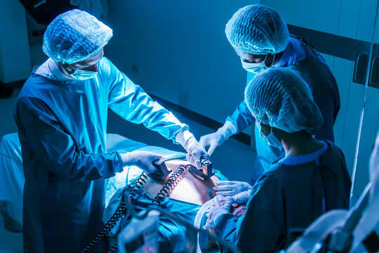 Team of surgeon doctor using defibrillator to give electrical shock to patient heart who is suffering from cardiac arrest in emergency surgical room for healthcare usage - Powered by Adobe
