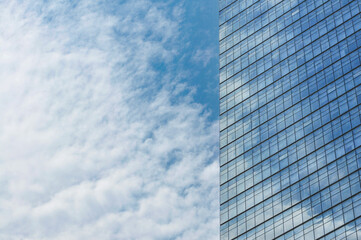 Glass mirror skyscraper wall with blue sky and white clouds reflection close up