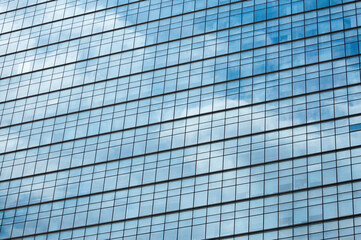 Glass mirror skyscraper wall with blue sky and white clouds reflection close up