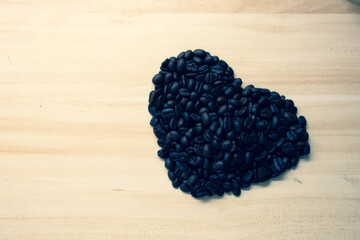 Roasted coffee beans arranged in heart shape on wood background.