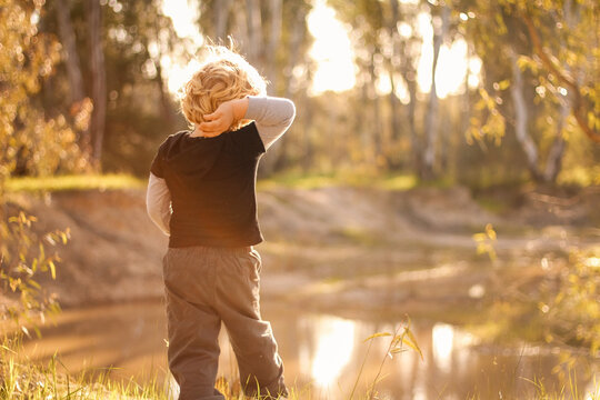 Little boy throwing rocks into water in the Australian bush in golden afternoon light