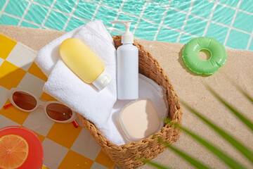 Poolside summer basket with towel, sunscreen, and cosmetic bottle on yellow checkered fabric, surrounded by tropical drinks and clear turquoise water, perfect for vacation product concepts.