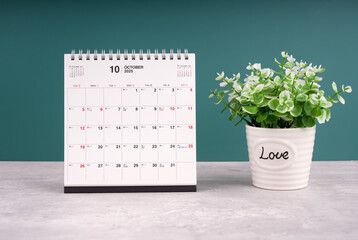 Desktop calendar for October 2025 on the table with plants pot.