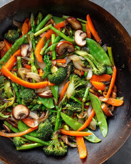 A close up shot of a vibrant vegetable stir fry in a dark wok with mixed ingredients