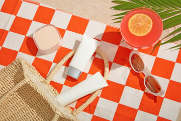 Orange checkered towel with white sunscreen tubes, sunglasses, cocktail, and tropical shadows,...