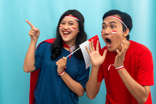 Indonesian Couple pointing and laughing together while holding a flag. Sharing joy on a day of national pride. - Powered by Adobe