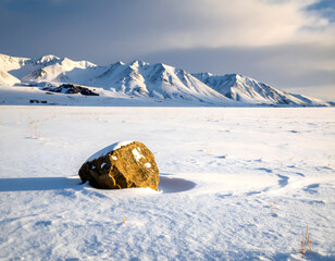 Single Rock in Snowy Plains with Mountain Background